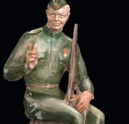 SOVIET PORCELAIN FIGURINE OF VASSILII TERKIN AS A SEATED YOUNG SOLDIER, DESIGNED BY ALEKSEI GEORGIEVICH, DULEVO PORCELAIN FACTORY, 1948